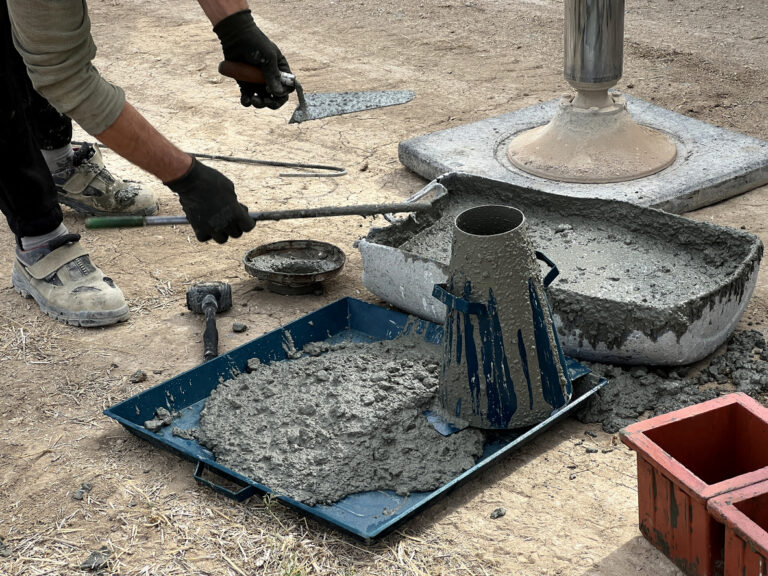 wet concrete in a tray alongside a conical apparatus for testing slump and a construction worker's hands reaching for it